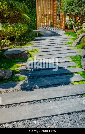 Particolare del percorso ardesia con pacciame di corteccia e piante native in giardino giapponese con patio in legno. Concetto di giardinaggio e di architettura paesaggistica. Foto Stock