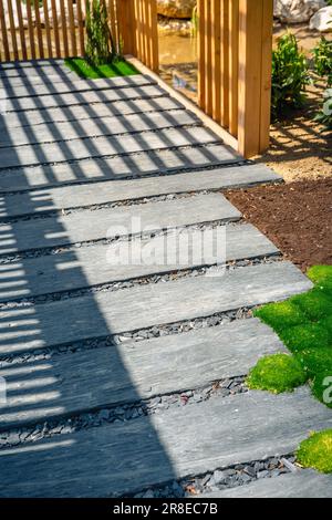 Particolare del percorso ardesia con pacciame di corteccia e piante native in giardino giapponese con patio in legno. Concetto di giardinaggio e di architettura paesaggistica. Foto Stock