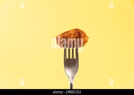 Croquette tradizionale spagnola fatta in casa su una forchetta su sfondo giallo isolato Foto Stock