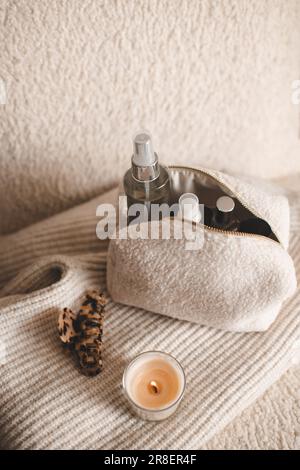 Soffice borsa cosmetica con prodotti cosmetici per il trucco e candela profumata su abiti a maglia in sedia closeup vista dall'alto. Foto Stock