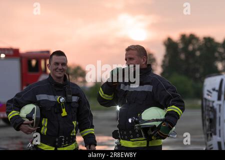 pompieri che utilizzano walkie talkie in azione di soccorso camion dei pompieri e la squadra di pompieri in background. Foto Stock