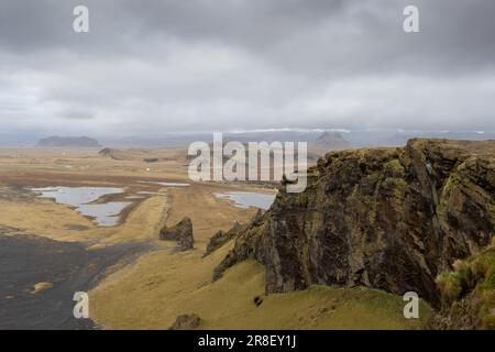 Paese sulla costa dell'oceano Atlantico. Piccolo lago circondato da montagne coperte di muschio e lichene in autunno. Cielo nuvoloso. Dyrholaey, sout Foto Stock