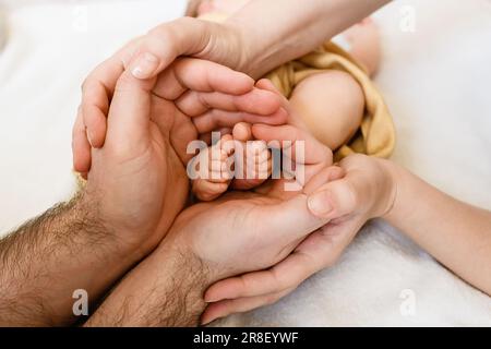 Le dita dei piedi del bambino piccolo nelle mani dei genitori, l'amore e l'unità della famiglia, la madre ed il padre tengono i piedi neonati del bambino, pelle alla pelle Foto Stock