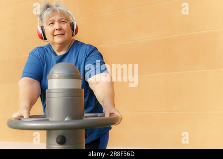 donna obesa attiva anziana in abbigliamento sportivo allenarsi su una palestra in una palestra del parco mentre si ascolta la musica con le cuffie Foto Stock