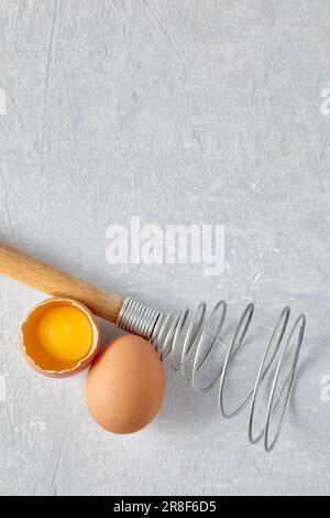 Due uova di pollo beige e una frusta rara per sbattere. Ingredienti di cottura isolati su sfondo bianco. Vista dall'alto con spazio di copia Foto Stock