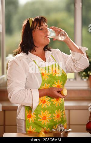 Donna che beve un bicchiere d'acqua con succo di limone, spremiagrumi, fascia per capelli, appena spremuto Foto Stock