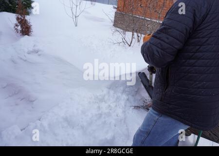 Un uomo pulisce la neve in inverno nel cortile della casa. Un uomo pulisce la neve con una pala Foto Stock