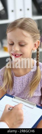 Amichevole medico pediatra donna che tiene appunti ascoltando la bambina Foto Stock