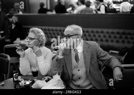 Fumatori all'interno di 1980s coppia britannica che guarda annoiato marito e moglie. Coventry Working Mens Club, sabato sera bingo intrattenimento serale. Marito e moglie hanno un 'moke' fumare sigarette. Coventry, Inghilterra circa 1981 UK 80s HOMER SYKES Foto Stock