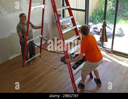 Amersfoort, Paesi Bassi - Giugno 11 2023 due uomini spostano una scala alta affittata in una stanza. Vogliono appendere una lampada ad un'altezza di 4 metri. La scala è fr Foto Stock