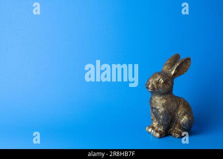 Figurina di coniglio d'oro su sfondo blu. Spazio libero Foto Stock