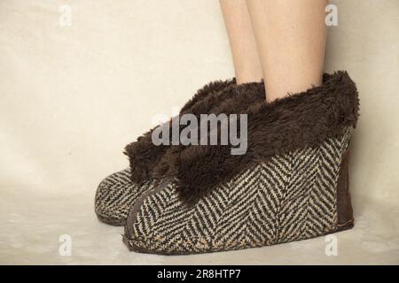 piedi femminili in caldo marrone pantofole casa su uno sfondo bianco, scarpe da casa Foto Stock