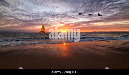 Una barca a vela sta navigando lungo l'oceano con Un'onda che si rompe sulla riva Foto Stock