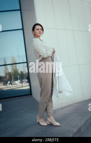 Ritratto di una bella giovane donna d'affari in piedi contro il centro ufficio, verticale Foto Stock