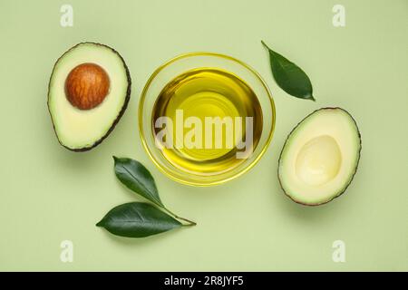 Ciotola con olio, avocado fresco tagliato e foglie su fondo verde chiaro, piatto Foto Stock