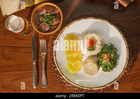 Bellissimo piatto di feijoada con birra. Sullo sfondo vecchi libri Foto Stock