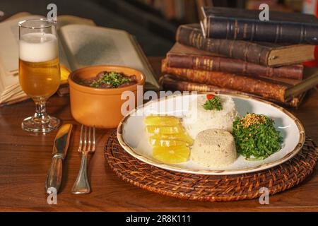 Bellissimo piatto di feijoada con birra. Sullo sfondo vecchi libri Foto Stock