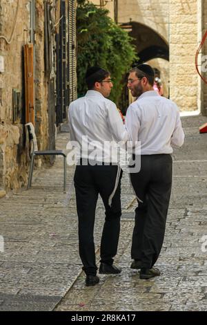 Due uomini ebrei che camminano e parlano su un marciapiede a Gerusalemme, Israele. Foto Stock