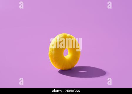 Singola fetta di ananas isolata su sfondo viola. Anello di ananas dalla luce brillante minimalista su un tavolo colorato. Foto Stock