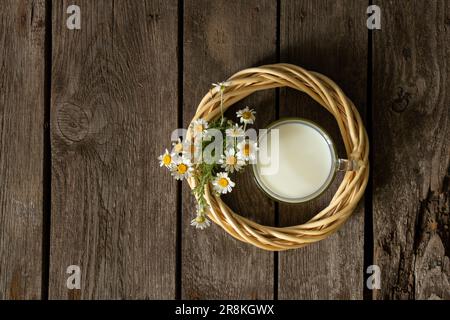 bicchiere di latte e margherite selvatiche su un tavolo al mattino Foto Stock