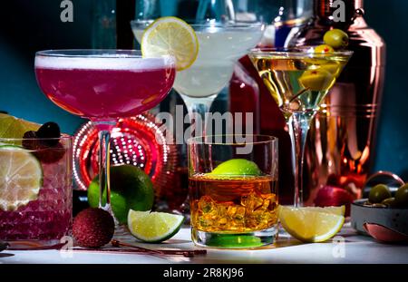 Cocktail alcolici, bevande forti e aperitivi, strumenti da bar, bottiglie su sfondo verde scuro, luce intensa. Martini vodka, signora rosa, aperol spritz Foto Stock