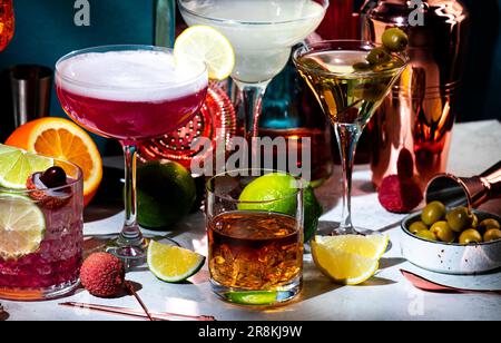 Cocktail alcolici, bevande forti e aperitivi, strumenti da bar, bottiglie su sfondo verde scuro, luce intensa. Martini vodka, signora rosa, aperol spritz Foto Stock