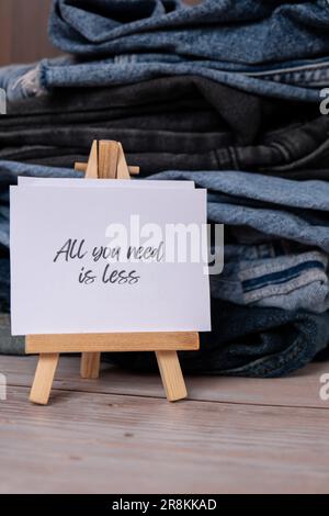 TUTTO CIÒ DI CUI HAI BISOGNO È MENO testo su carta nota su Jeans assortimento abbigliamento shopping sostenibile di seconda mano. Armadio a capsula minimal. Consumo eccessivo di moda sostenibile, consumo di acquisto cosciente, concetto di idea di modo lento. Stile di vita a basso contenuto di rifiuti Foto Stock