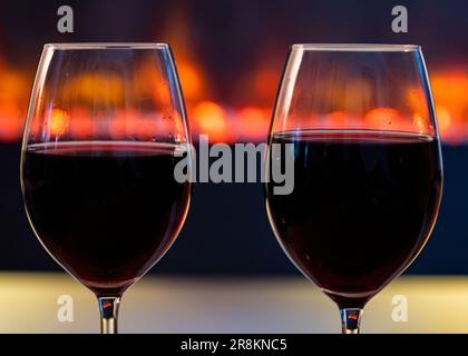 Due generosi bicchieri di vino rosso davanti a un fuoco soffice e luminoso caminetto Foto Stock