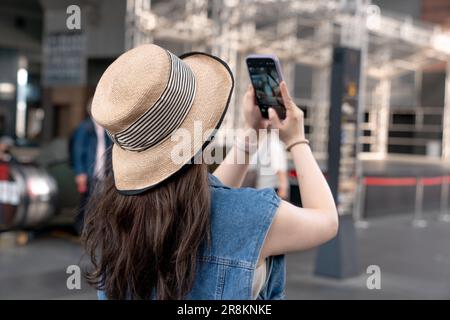 Una giovane donna in un cappello di paglia, scattando foto con il suo telefono Foto Stock