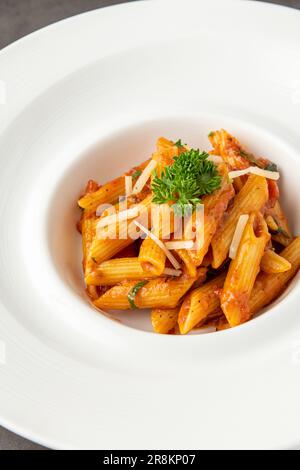 Penne in salsa di pomodoro, pomodori decorati con prezzemolo su fondo di legno Foto Stock