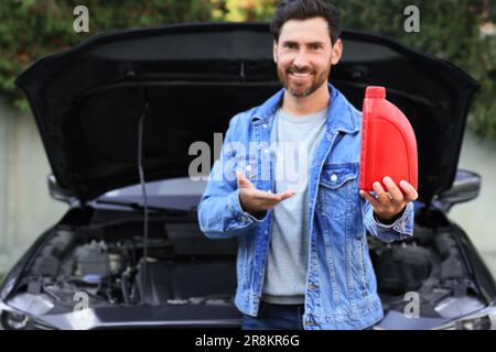 Uomo sorridente che mostra olio motore vicino auto all'aperto, concentrarsi sul contenitore rosso Foto Stock