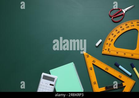 Composizione piatta con goniometro, triangolo e cancelleria su lavagna verde. Spazio per il testo Foto Stock