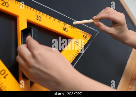 Donna che disegna con gesso e righello triangolare su lavagna, primo piano Foto Stock