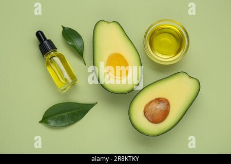 Olio essenziale, avocado fresco tagliato e foglie su fondo verde chiaro, piatto Foto Stock