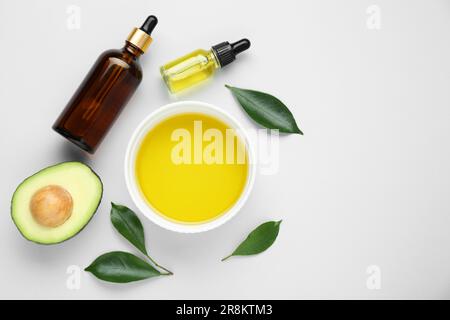 Olio essenziale, avocado fresco tagliato e foglie su fondo bianco, piatto. Spazio per il testo Foto Stock