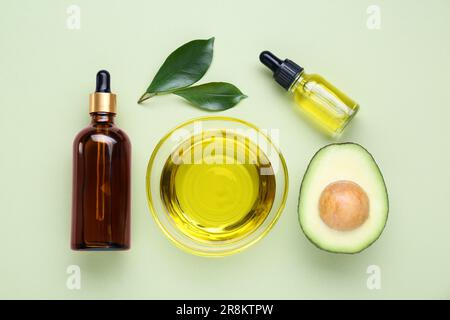 Olio essenziale, avocado fresco tagliato e foglie su fondo verde chiaro, piatto Foto Stock