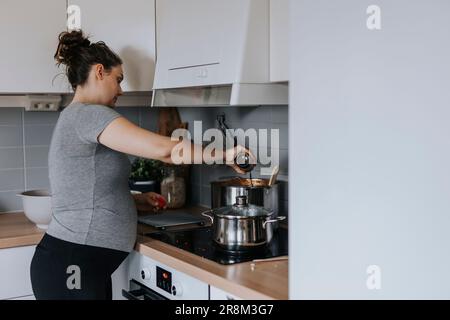 Donna incinta in cucina che prepara il cibo Foto Stock