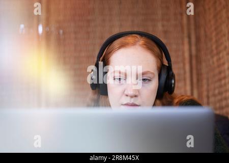 Giovane donna che indossa cuffie che ascolta musica o podcast mentre studia con un notebook Foto Stock