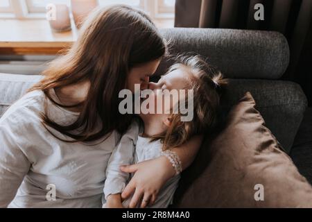 Mamma abbraccia e bacia bambino disabile sul divano Foto Stock