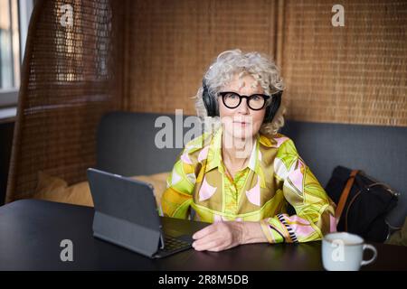 Ritratto di una donna anziana con cuffie che utilizza un tablet Foto Stock