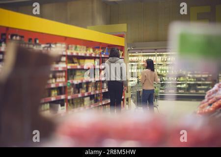 Vista posteriore di una coppia che si trova di fronte agli scaffali del supermercato e che fa shopping insieme Foto Stock