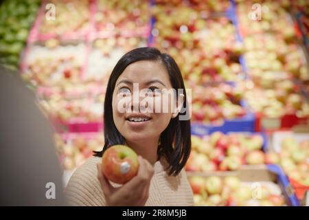 Donna sorridente in un supermercato con mela rossa e gialla Foto Stock