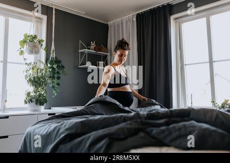 Donna incinta che fa i lavori di casa e fa il letto la mattina Foto Stock