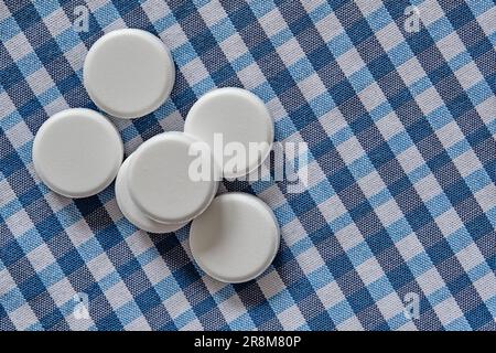 Una pila di compresse rotonde di farmaci farmaceutici su un panno di tessuto a scacchi bianco-blu. Vista dall'alto di una pila di integratori alimentari. Foto Stock