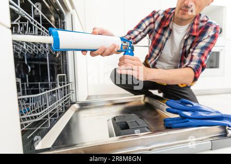 Addetto alla manutenzione che ripara la lavastoviglie in una cucina moderna. Concetto di manutenzione e assistenza domestica Foto Stock