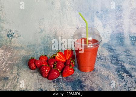 Fragole rosse mature e frullato di fragole in un bicchiere trasparente su sfondo blu Foto Stock