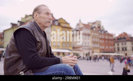 Senior siede sui gradini e visita turistica tenendo in mano uno smartphone nel centro storico di una vecchia città europea. Piazza del Palazzo, centro storico di Varsavia Foto Stock