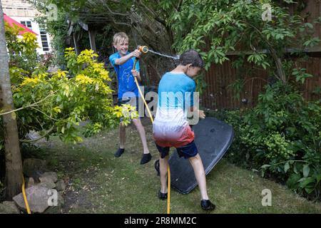 I ragazzi che hanno una lotta per l'acqua utilizzando un tubo flessibile nel loro giardino residenziale nel sud-ovest di Londra, Inghilterra, Regno Unito Foto Stock