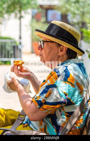 Donna anziana matura in cappello di paglia sul centro città panca giardino mangiare un dolce - Tours, Indre-et-Loire (37), Francia. Foto Stock