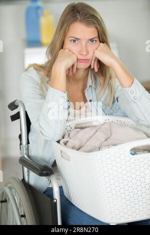 donna sconvolta in sedia a rotelle facendo il suo bucato Foto Stock